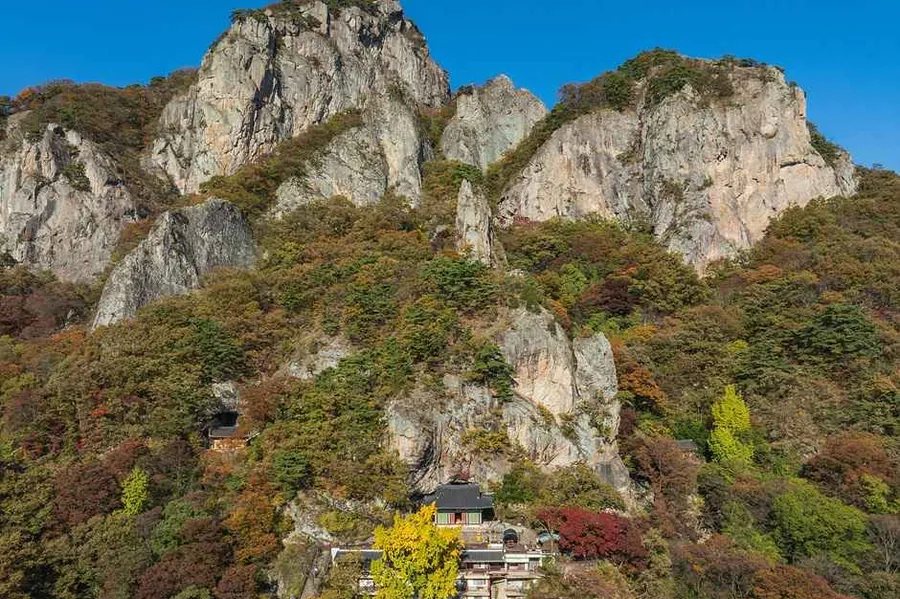 백학봉의 흰 바위 절벽과 그 아래 비탈에 앉은 암자 건물