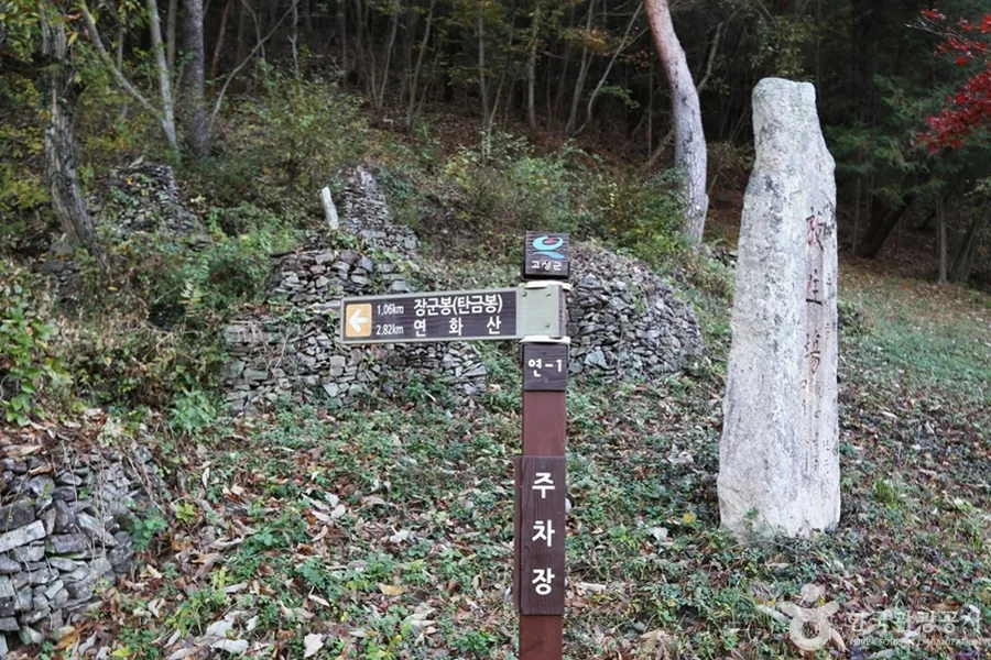 돌담 앞에 선 목재 이정표와 그 옆의 오래된 비석
