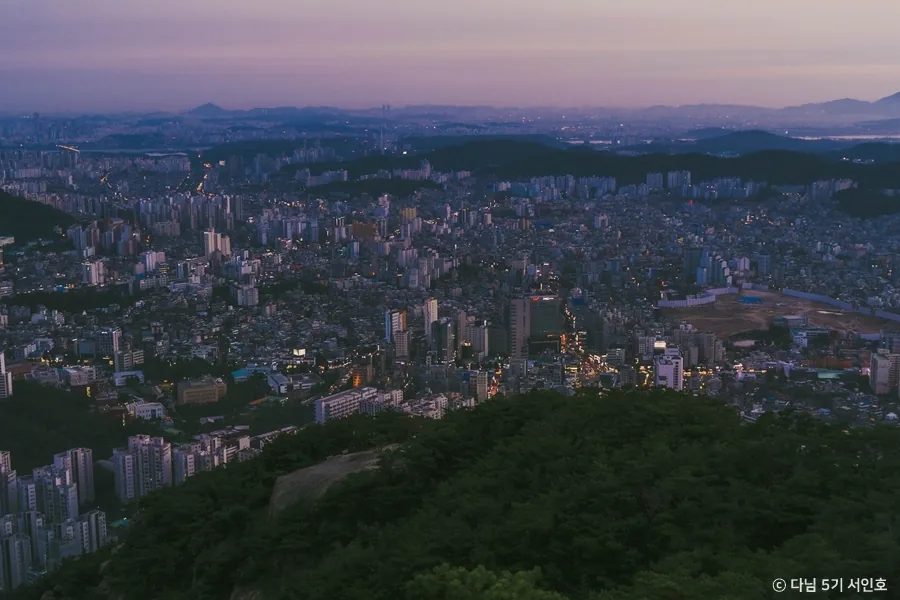 Seoul spread out below a wooded Bukhansan ridge at dusk